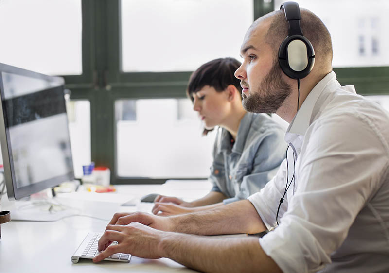 A man wearing headphones at a computer in a contact centre