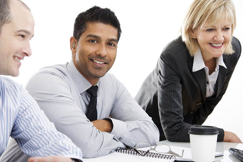 Smiling business people in a meeting. The man in the middle is wearing a hearing aid.