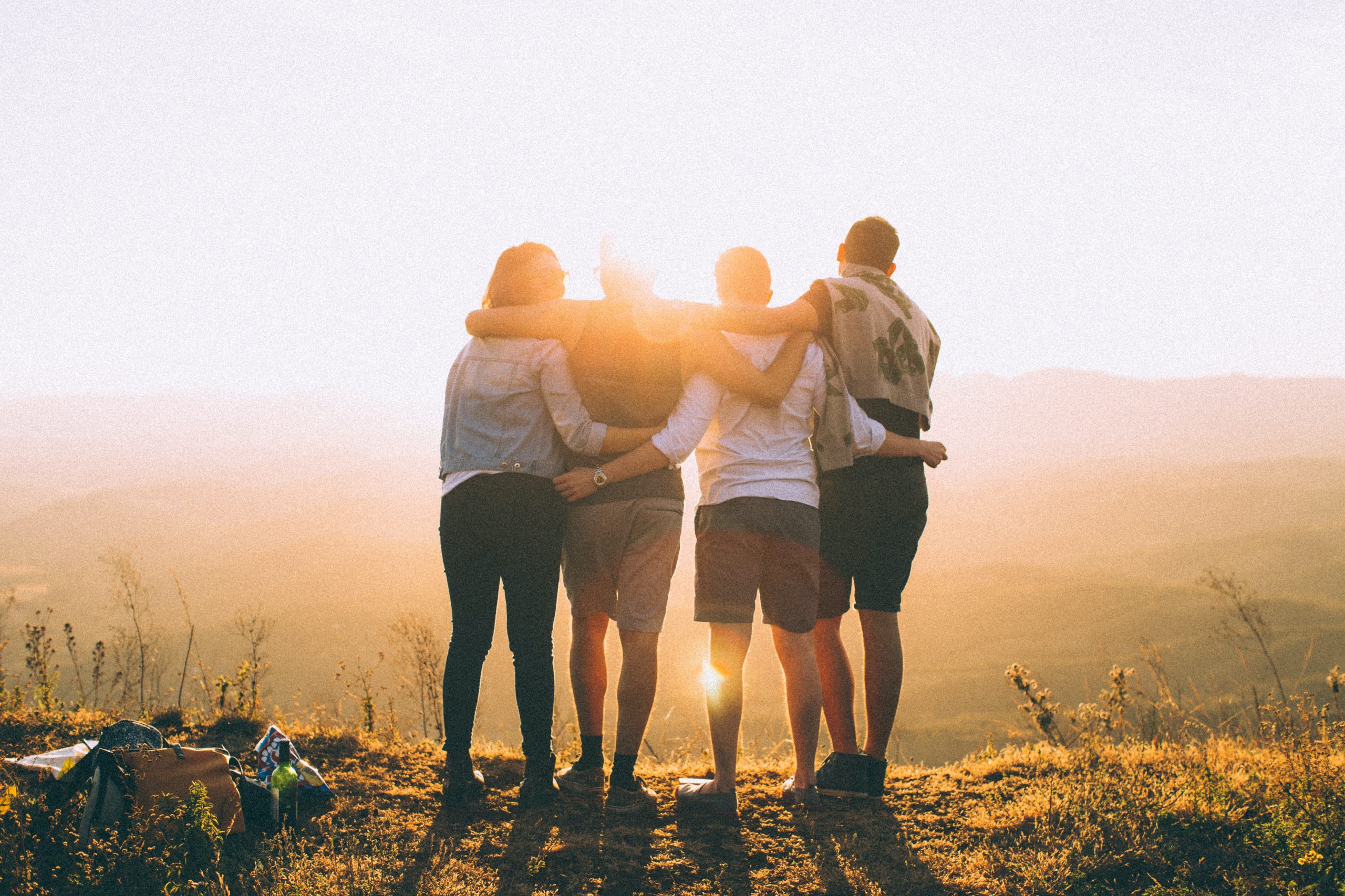 Four people with their arms around each other, standing on a mountain watching the sunset