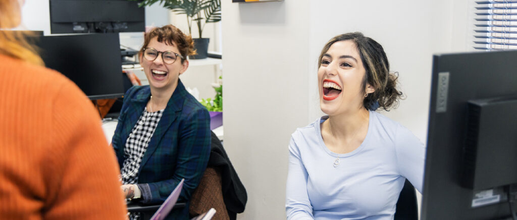 Three women interacting and laughing in an office space 