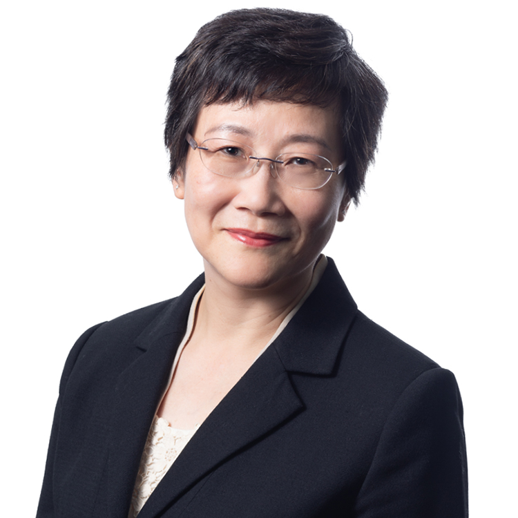 Rida is a woman with short black hair. She is wearing glasses, a black blazer and white top. She is smiling.